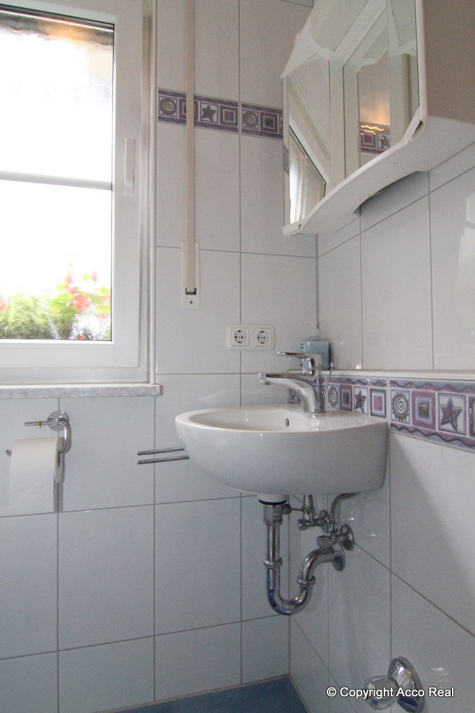 Waschbecken mit Spiegel unter einer Leuchte in einem weiß gefliesten Badezimmer mit Fenster.